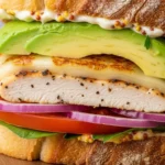 Close-up of a delicious Chicken Avocado Melt sandwich with melted Swiss cheese and creamy avocado.