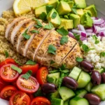 Close-up of a vibrant Mediterranean chicken bowl filled with grilled chicken, colorful vegetables, and a lemon wedge.