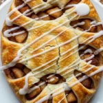 Close-up of a warm, golden Apple Kringle pastry filled with spiced apples and drizzled with vanilla glaze. Perfect homemade dessert!