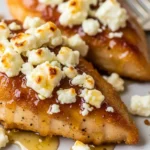 Close-up of golden brown crispy hot honey chicken topped with crumbled feta cheese.
